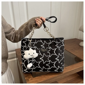 Détail d'un sac cabas noir avec broderie d'étoiles, chaîne dorée et breloque nuage
