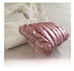 Detail of soft quilted metallic pink puffer clutch bag with glossy cloud texture