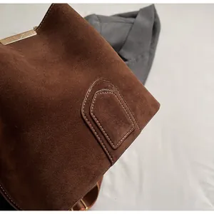Detail of premium brown suede bucket bag featuring high-quality stitching and gold metal clasp