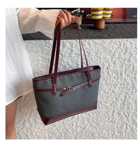 Detail of grey woven tote bag with burgundy leather trim and metallic eyelet buckle