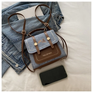 Detail view of denim backpack with brown leather strap and simple cat print decoration