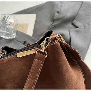 Detailed close-up of premium brown suede bucket bag featuring a sturdy gold metal hook clasp