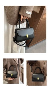 Detail of a black leather handbag with gold metal clasp and adjustable shoulder strap