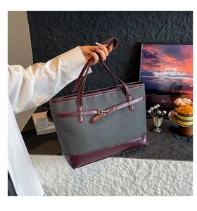 Detail of grey woven tote bag with burgundy leather handles and metal buckle accent