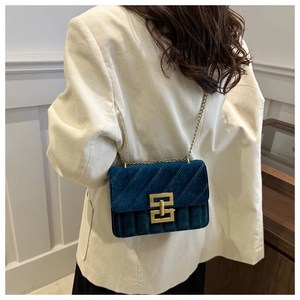 Detailed view of dark blue velvet quilted bag with gold chain and metal buckle on model