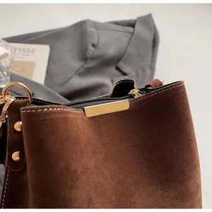 Detailed close-up of dark brown suede bucket bag with premium gold hardware and white stitching