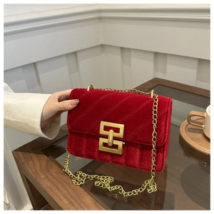 Close-up of red velvet quilted bag with golden square lock and elegant chain strap