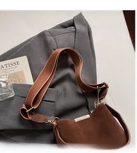 Detail of a brown suede bucket bag with adjustable woven strap on a grey blazer