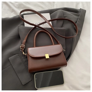 Close-up of vintage brown crossbody bag on grey blazer with gold metal buckle detail