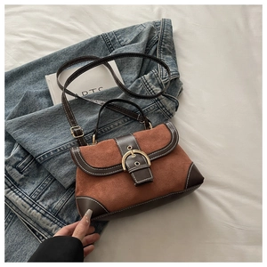 Close-up of brown suede handbag featuring a large gold horseshoe buckle and top handle