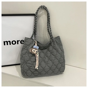 Close-up of heart-quilted grey tote bag featuring a woven handle and plush bear charm