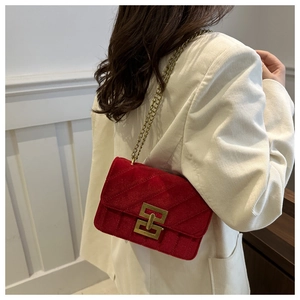 Detail of red quilted velvet handbag with gold chain strap worn on white corduroy jacket