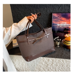 Detail of a brown woven tote bag with smooth leather trim and buckle design