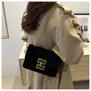 Detail of black velvet crossbody bag with gold chain and metal lock worn with a trench coat