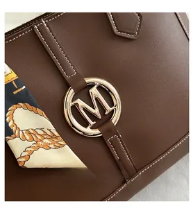 Detail of brown leather tote featuring a gold M-logo and decorative printed silk scarf