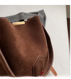 Detail of dark brown suede bucket bag with gold metal closure and stitching
