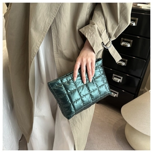 Detail of dark green quilted metallic clutch held by a model wearing a khaki trench coat