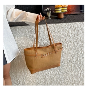 Detail of a brown woven tote bag featuring contrast faux leather trim and metallic buckles