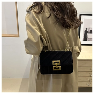 Close-up of black velvet crossbody bag with gold chain and embroidery on beige coat