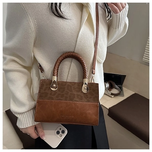 Detail view of the brown leather handbag with leopard print and woven handle on a desk