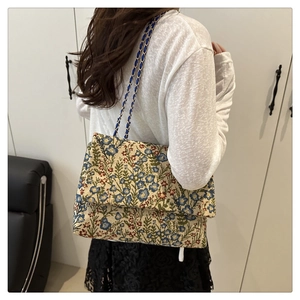 Schultertasche mit Blumenmuster und Kettenriemen am Model in häuslicher Umgebung