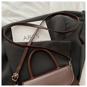 Detailed view of deep brown vintage leather bag placed on a black blazer jacket