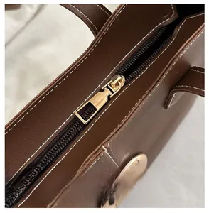 Close-up of brown textured leather tote bag showing high-quality stitching and golden zipper