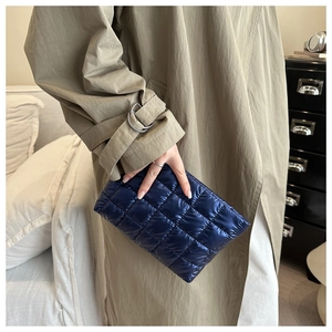 Détail d'un sac à main matelassé bleu foncé tenu contre un trench-coat kaki en intérieur