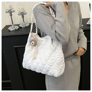 Detail of white quilted heart pattern shoulder bag with woven handle and plush charm