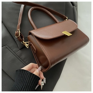 Detail shot of brown PU leather shoulder bag with gold clasp on black blazer background