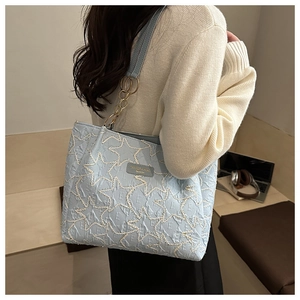 Détail du sac cabas bleu clair étoilé avec chaîne dorée sur l'épaule d'un mannequin