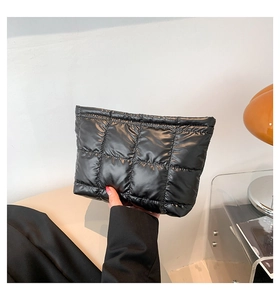 Détail d'une pochette matelassée noire en nylon brillant tenue par une personne