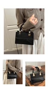 Detail of black crossbody bag with woven handle and gold hardware on glass table