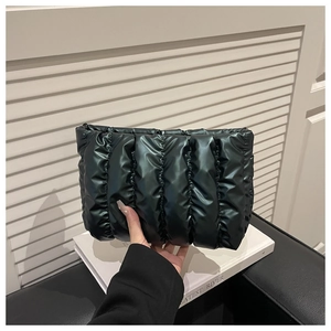 Detail of black glossy quilted cloud bag with padded vertical stripes held by hand