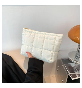 Détail d'une pochette matelassée blanche en nylon avec fermeture éclair dorée et grille