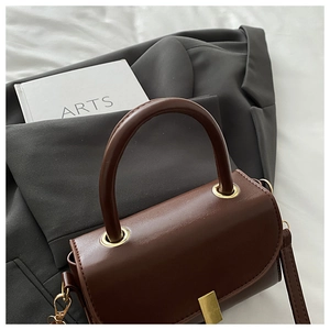 Detail view of brown vintage leather handbag with gold buckle and top handle on blazer
