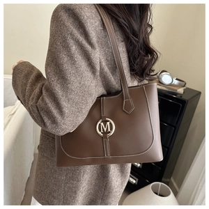 Close-up of brown leather tote bag with white contrast stitching and gold 'M' logo