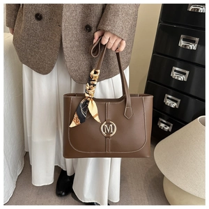 Detail of brown leather tote bag with M-logo, contrast stitching and silk scarf wrap