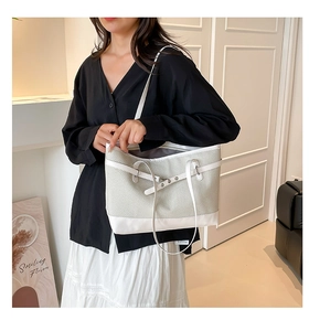 Detail of grey woven tote bag with white leather trim and elegant metal buckle accents