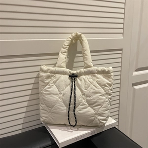 Cream quilted tote bag with heart embroidery and drawstring detail on white book