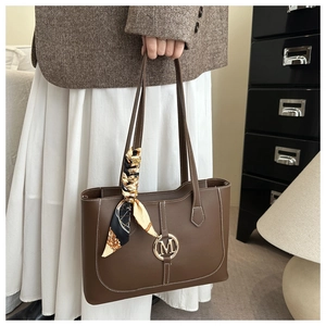 Detail of coffee brown leather tote bag with M-logo and decorative silk scarf on the handle