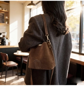 Brown suede bucket bag detail with golden hardware on a tweed coat in warm daylight