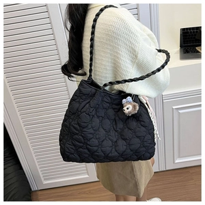 Detail view of black quilted tote bag with woven straps and plush charm on the side