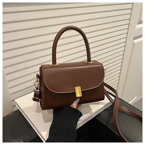 Detail view of a vintage brown leather handbag with a gold metallic buckle on white books