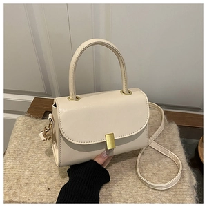 Detail of cream white leather handbag with gold buckle and top handle in warm lighting