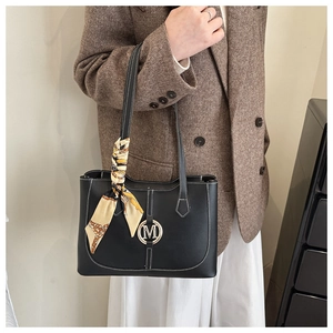 Detail of black leather tote bag featuring gold M logo and decorative silk scarf on handle
