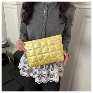 Détail d'une pochette matelassée jaune vif au fini satiné métallique tenue par un modèle