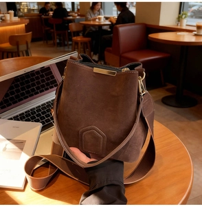 Detail of dark brown suede bucket bag with gold metal trim on a wooden table