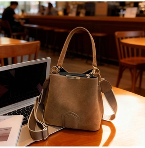 Close-up of vintage brown suede bucket bag with wide shoulder strap on wooden desk