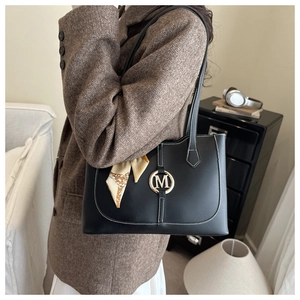 Detail of black leather tote bag with silk scarf handle and metal M logo on the front